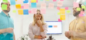 woman standing in the middle of two men looking pensive facing a glass wall filled with colorful sticky notes