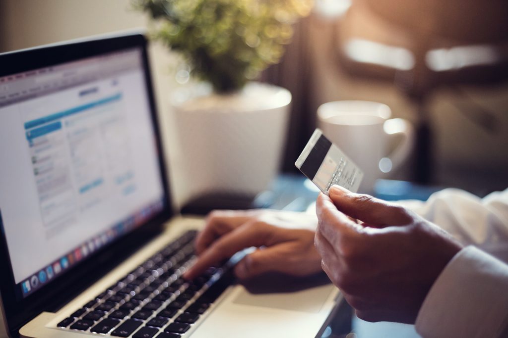 hands rest on a computer while holding a credit card prepared to make an online purchase from an ecommerce website