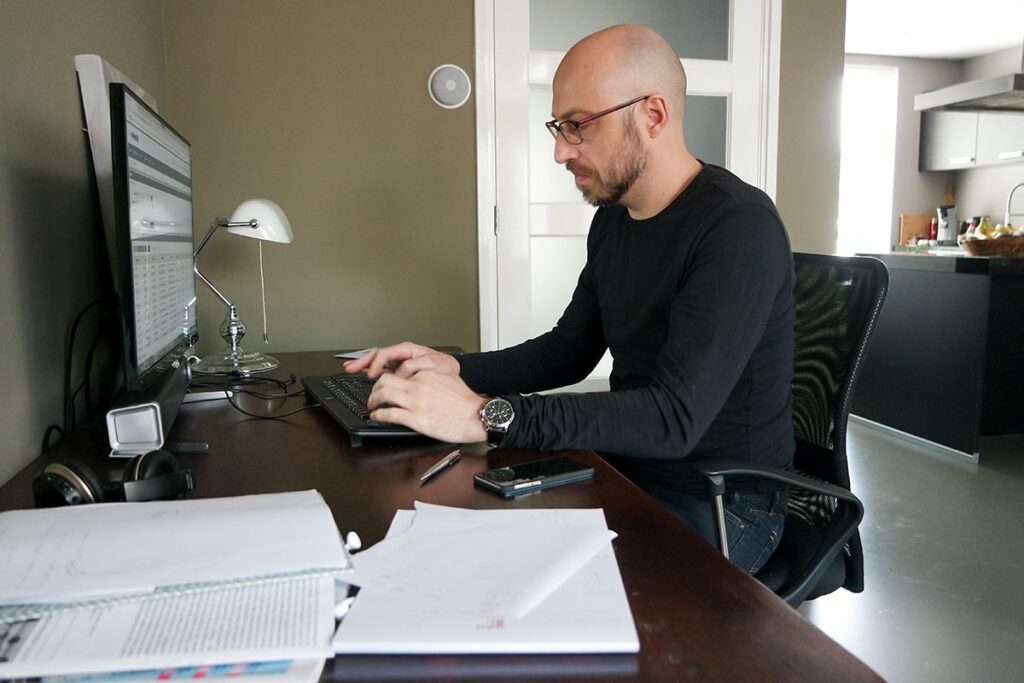 a man works at a home office desk, with papers scattered about, while writing a blog with seo tips