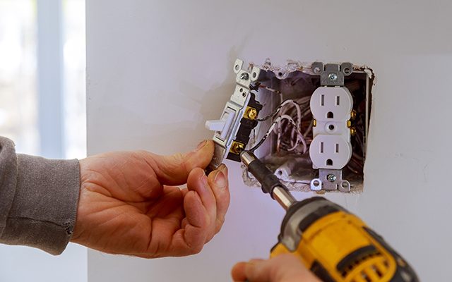 The hands of an electrician installing a power switch to the electrical junction box