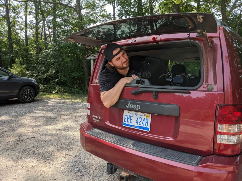 a photographer peers out the back of a vehicle, ready to take pictures