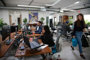 a woman walks through a busy office space with people working on computers