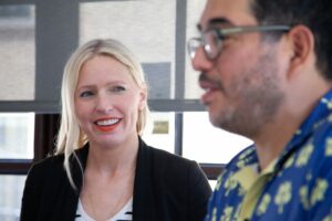 a female marketer looks at her coworker, a male marketer wearing glasses, while he searches his computer