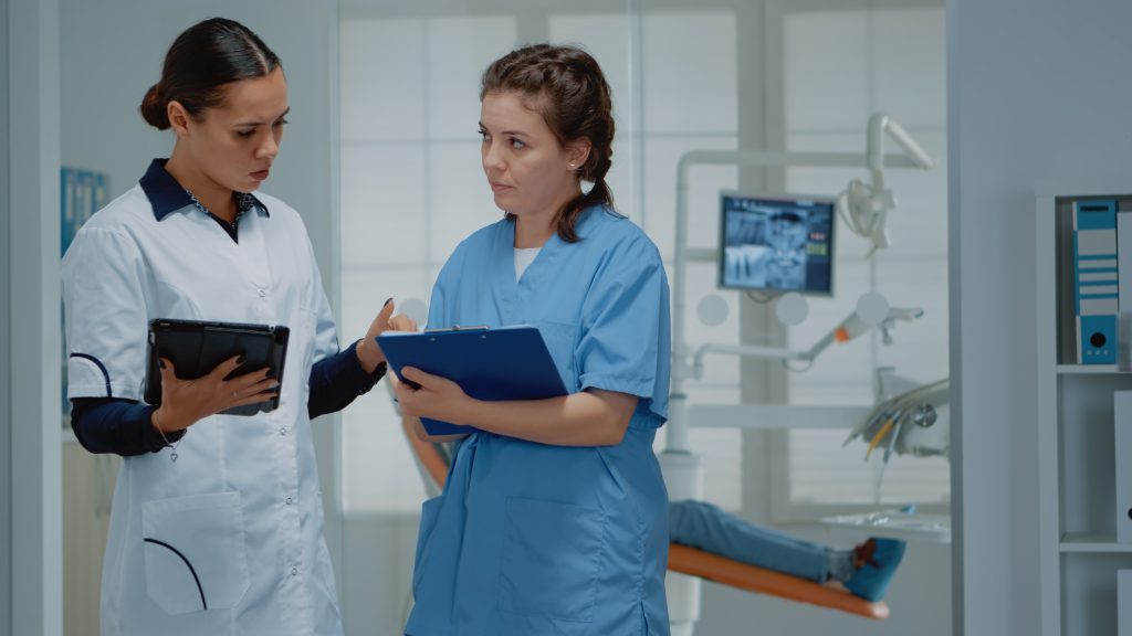 two dentists working team discussing dental operation at clinic. Dentist and assistant standing in stomatological cabinet while talking about oral equipment and teeth examination