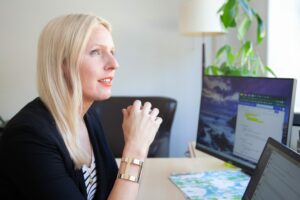 female marketer looks out of the office window with several computer screens on a desk in front of her, her hands are folded and rested on the desk thinking of how to brand her ecommerce business