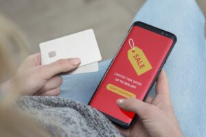 top down view of a woman holder her credit card in her left hand and a mobile phone with the word "sale" on it in her right hand, apparently making a purchase for an online sale