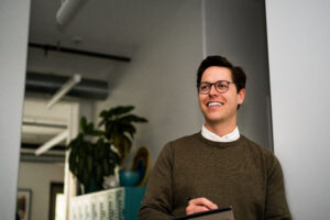 a marketer stands in a well lit office, seen from a slightly low angle holding a notebook and pen