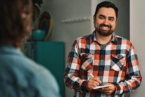 a marketing employee leans on a wall with a notebook in hand while talking to another employee