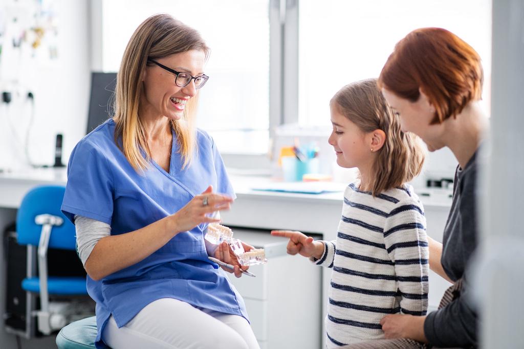 A female dentist explains a procedure to a child and her parent.