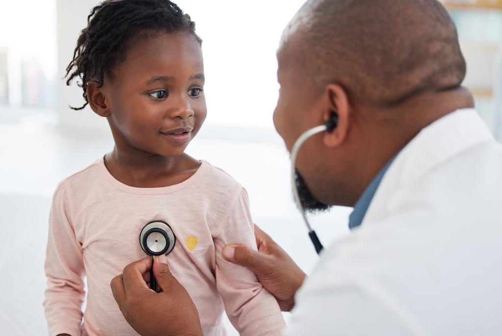 A doctor listens to the heartbeat of a smiling child.