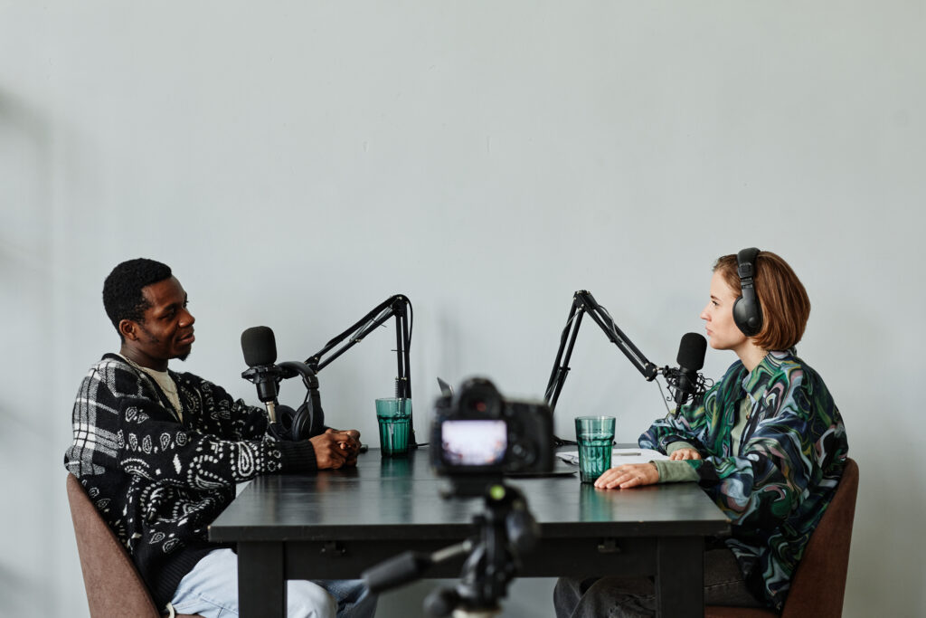 Side view portrait of two people speaking to microphones while recording podcast in studio